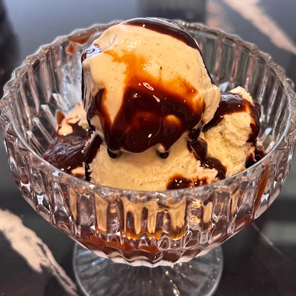 Scoops of vanilla ice cream drizzled with chocolate sauce in a faceted glass dessert dish.