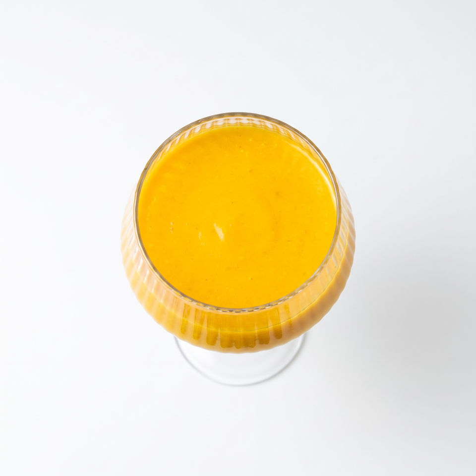 Overhead view of smooth bright orange sauce served in a decorative glass bowl against a white background.